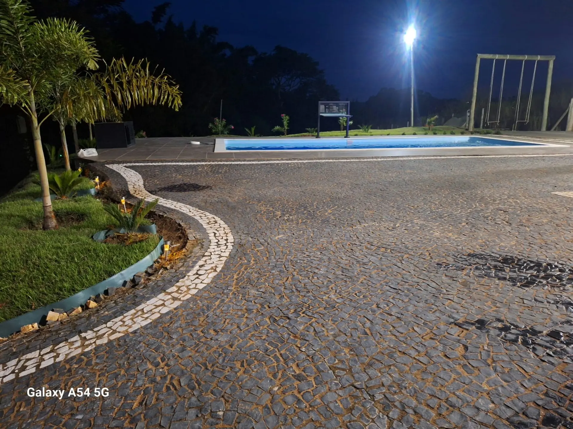 Área de lazer iluminada à noite com piscina e jardim